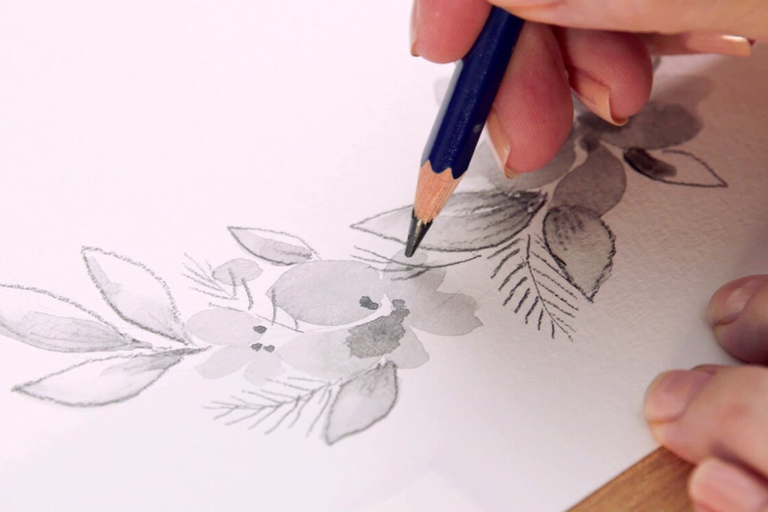uma mão desenha uma grinalda de flores com um lápis de grafite aguarelável