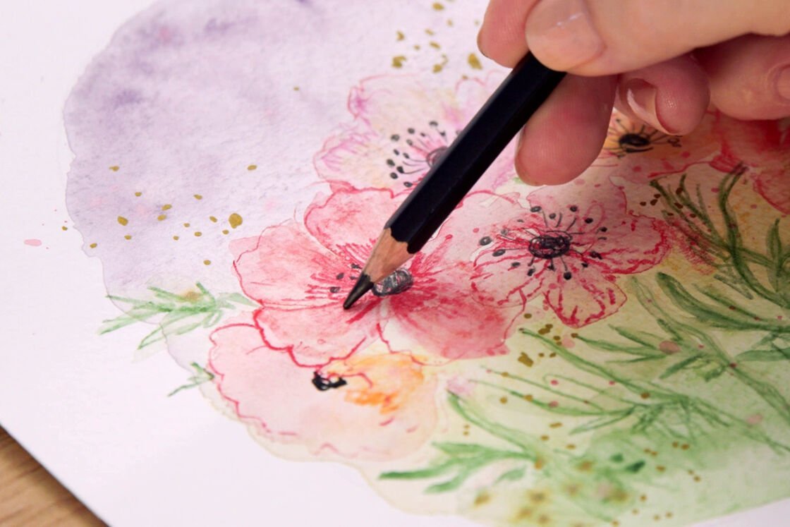 a hand draws a flower meadow with a watercolour pencil