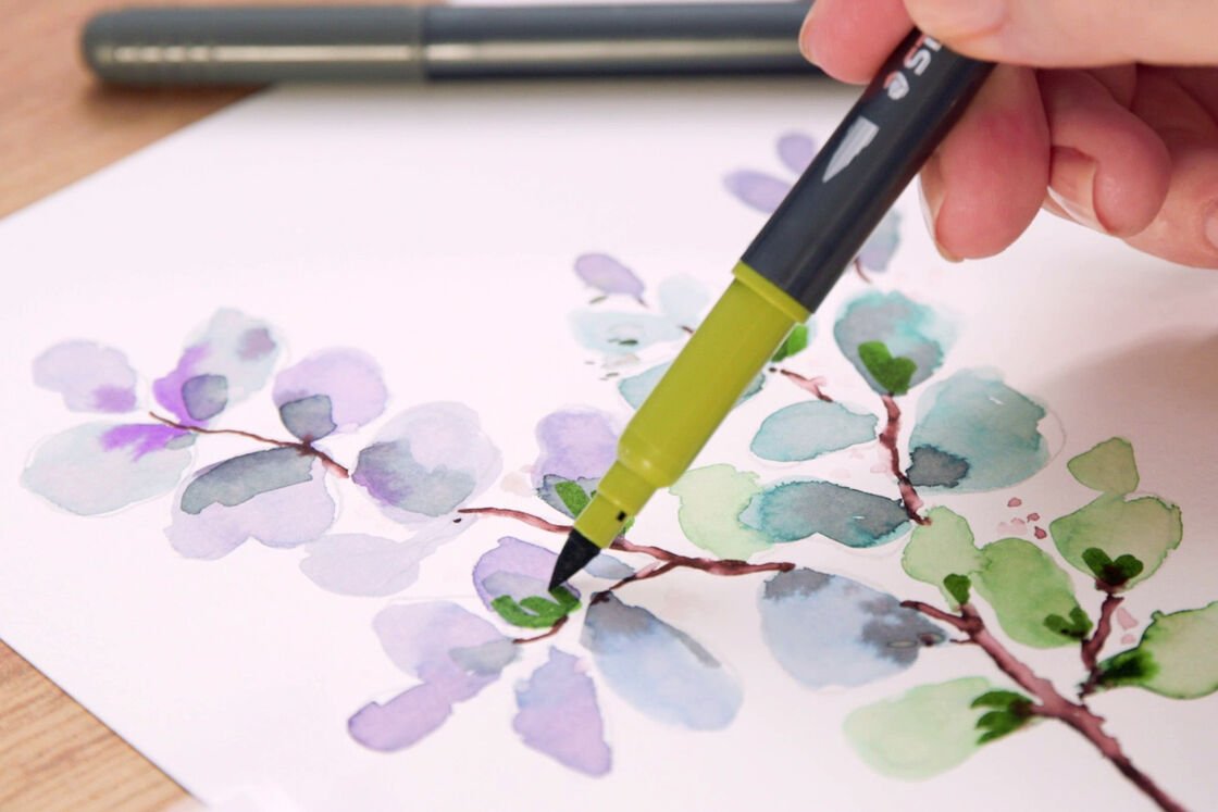 a hand draws different coloured leaves with a brush pencil